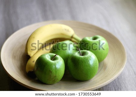 Wooden bowl with green apples and bananas on a table. Selective focus.