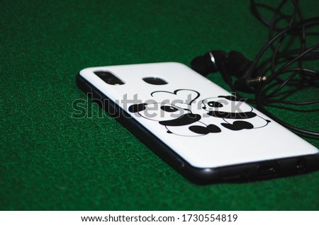 Phone with cartoon case and earphone on a green background