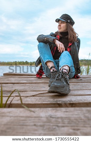 young stylish woman sitting on wooden pier with lake on background