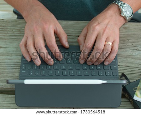Man typing on tablet outside at a picnic table. This picture was taken outside during the corona virus pandemic when many people needed to work from home. 