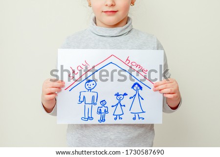 Little girl is holding a picture of family silhouette under the roof and words Stay Home on yellow background. Children in quarantine concept.