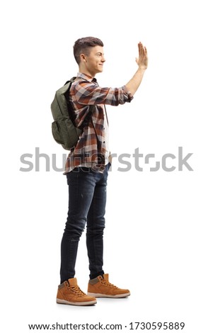 Full length profile shot of a male student with a backpack gesturing high-five isolated on white background