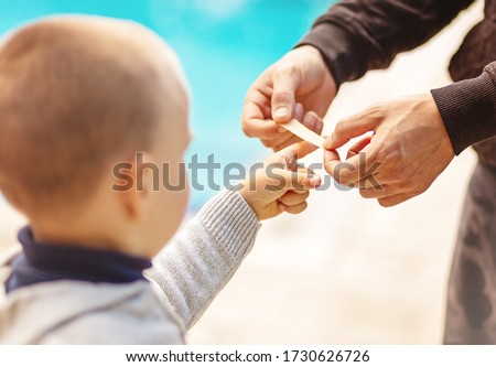 Dad putting a plater band-aid on his sons finger on white background, close-up, no face recognizable Royalty-Free Stock Photo #1730626726