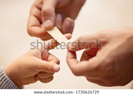 Dad putting a plater band-aid on his sons finger on white background, close-up, hands only