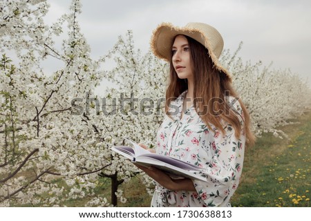 Girl reading a book in the spring garden. Gorgeous woman in hat and dress on nature. Camping with a book. Spring. Summer.