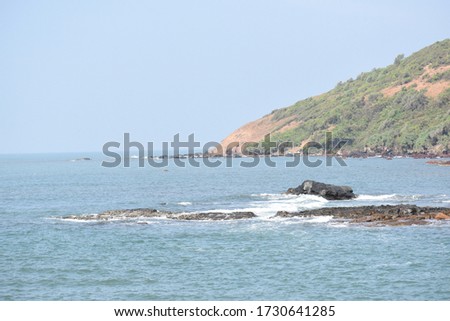 Black rocks in the seashore and mountain in the background..A view from Goa beach.