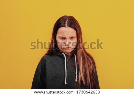 Very angry, upset girl looking at the camera. Portrait of a beautiful girl closeup. Orange background. Grey bike with the laces. Long blond hair.