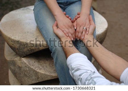 Young couple together, hands on top of each other, detail photo with rings in white top in a city park.