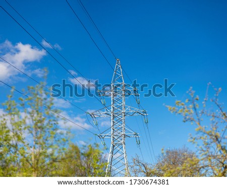 High voltage power lines against a blue sky and white clouds. Summer sunny day, landscape in the city park.