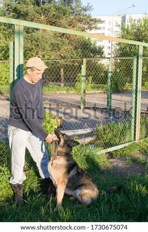 A man on a walk with a dog, in the city. German shepherd likes to walk with the owner, at sunset. It's a cool may evening outside.