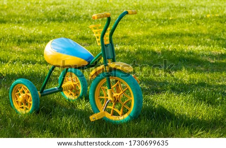 Small yellow and green children's tricycle standing on the grass on a sunny day. Copy space Royalty-Free Stock Photo #1730699635