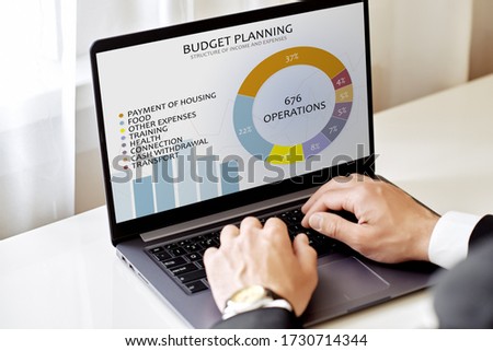 tracking finances concept. man with laptop plans budget looking at infographics on screen