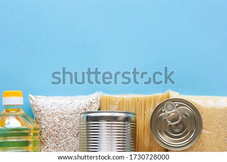 Set of grocery items from pasta, oatmeal, couscous, oil and canned food on blue background top view. Food delivery, donation concept. Food stock for quarantine. Copy space.