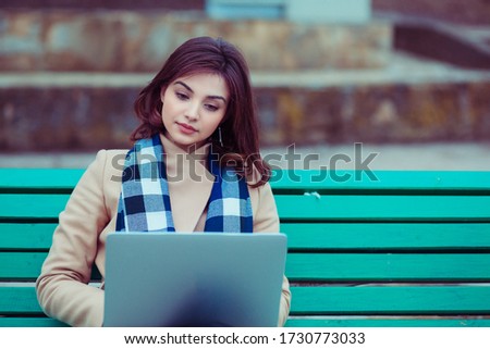 Russian asian girl, mixed race American woman outside sitting on a bench using laptop, outdoors in a city park.
