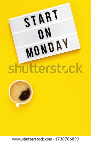 Text "start on monday" on lightbox and cup of coffee. Concept of new beginning. Top view on yellow background.