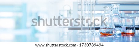 water and orange solution in glass flask and cylinder in soft blue light research medical science laboratory banner background Royalty-Free Stock Photo #1730789494