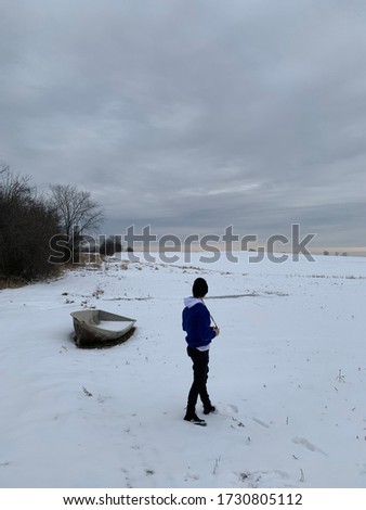 Person with camera standing in snow covered field with an abandoned boat 