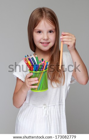 Happy little girl drawing with pencils on gray background on Education