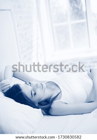 Portrait of sleeping attractive brunette girl at bedroom. Black and white monochrome blue tone picture.