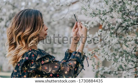 smiling girl photographs a blossoming cherry on a smartphone. young girl takes a selfie near sakura