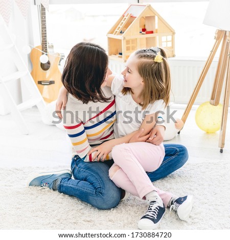 Beautiful mother kissing cute little girl in bright kids room