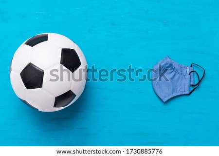 Soccer ball and medical mask on wooden blue with copy space. Safe sport concept
