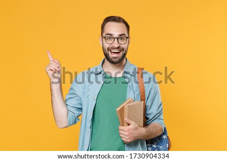 Excited man student in casual clothes glasses with backpack hold books isolated on yellow background. Education in high school university college concept. Mock up copy space. Pointing index finger up Royalty-Free Stock Photo #1730904334