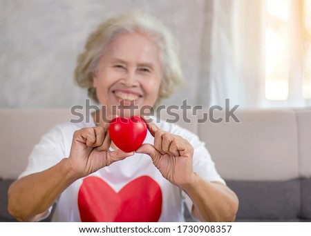 beautiful senior woman with a red heart in her hand She is smiling, bright, happy and in good health.