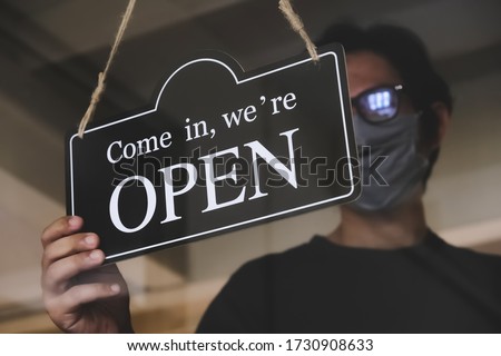 the state allows retail stores or restaurants and businesses to reopen after coronavirus restrictions. man with face mask turning a sign on a door shop. economy starts running after being on lockdown. Royalty-Free Stock Photo #1730908633