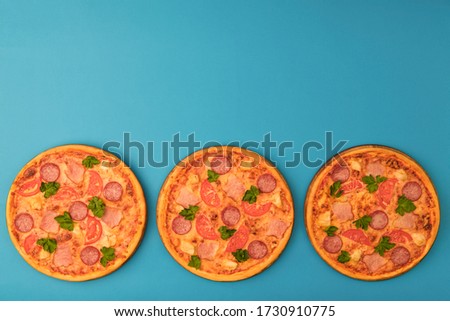 Three pizzas on the blue azure background. Pizza isolated. Design banner with copy space for text or logo. Italian cuisine. Meat and cheese pizza.