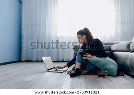 cozy young attractive girl at home working with a laptop and talking on the phone. comfort and coziness while at home. home office and work from home. remote online employment.