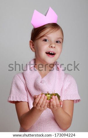 Image emotional joyful young girl with a beautiful smile in a knitted dress with a crown holding a gift on a gray background on Holiday/Little girl princess