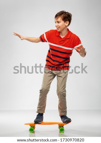 leisure, sport and people concept - happy smiling boy riding on short skateboard over grey background