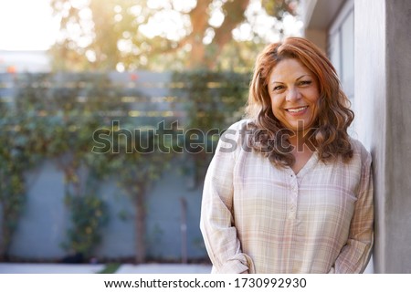 Portrait Of Smiling Senior Hispanic Woman In Garden At Home Against Flaring Sun Royalty-Free Stock Photo #1730992930