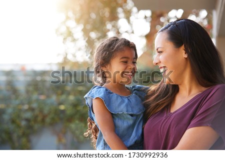 Smiling Hispanic Mother Holding Daughter Laughing In Garden At Home Royalty-Free Stock Photo #1730992936
