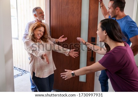 Couple Greeting Senior Parents At Front Door As They Come To Visit Royalty-Free Stock Photo #1730997931