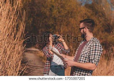 Couple of tourists reading a map in search for a hiking trail, having fun on summertime adventure trip and taking photos