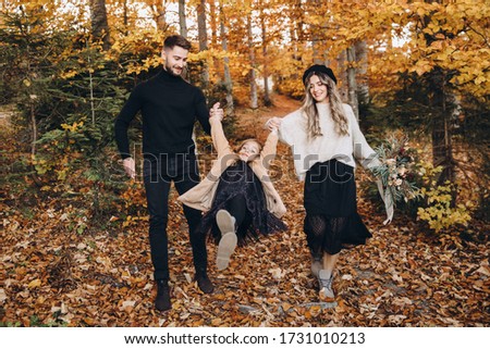 Stylish family in the autumn forest. A young guy and a girl are walking along a forest road among yellow leaves with their daughter.