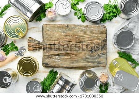 Canned food in tin jars on white wooden background. Top view.
