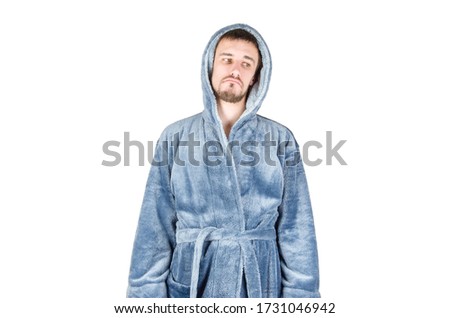 Portrait of young caucasian bearded man in blue bathrobe shows sad emotion on white background