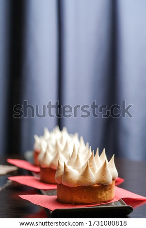 Tartlets with lemon curd and meringue on a serving plate on a dark background copy space.