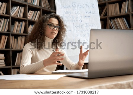 Female young hispanic school math teacher, college tutor coach looking at webcam and talking in classroom giving virtual teaching remote class online lesson by zoom conference call on laptop computer. Royalty-Free Stock Photo #1731088219