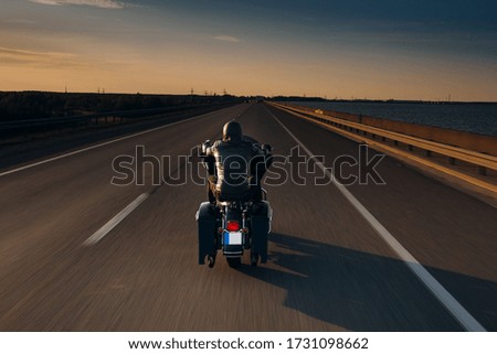 An Awe-Inspiring Shot of a Solo Motorcycle Rider Speeding along an Open, Vast Asphalt Motorway, Emphasizing the Thrill and Freedom of the Open Road on a Long, Straight Driveway Royalty-Free Stock Photo #1731098662