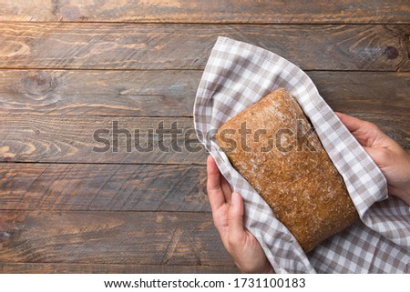 Young woman baker holds in hands sourdough bran whole grain bread loaf with walnuts in checkered cotton towel on rustic wood kitchen table. Baking local food specialties concept Royalty-Free Stock Photo #1731100183