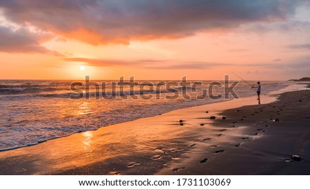 Silhouette of a fisherman fishing at beautiful sunset sunrise and ocean waves on Canggu Jimbaran Sanur beach, Bali Indonesia
