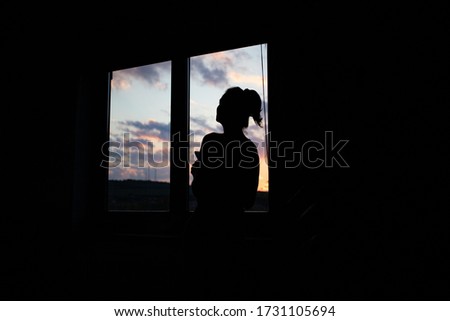woman silhouette watching sunset from window quarantine concept