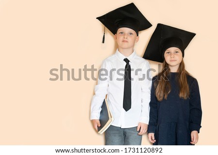 Graduation day! School children in graduation caps hugging each other isolated on beige studio background. Children and education 