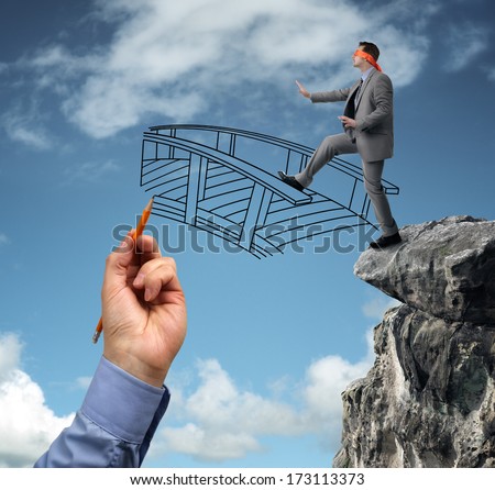 Businessman in a blindfold stepping off a cliff ledge with giant hand drawing a bridge for a safe crossing concept for building bridges, risk, challenge, conquering adversity, ignorance and assistance Royalty-Free Stock Photo #173113373