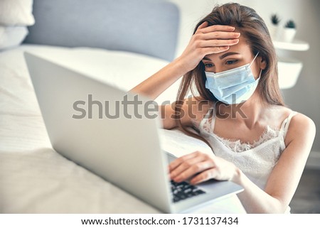 Young confused woman buying some goods on Internet at home while sitting in bedroom