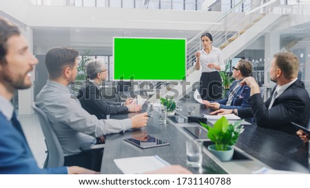 In the Corporate Meeting Room: Female Speaker Uses Digital Chroma Key Interactive Whiteboard for Presentation to a Board of Executives, Lawyers, Investors. Green Mock-up Screen in Horizontal Mode